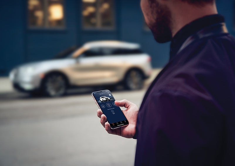 A person is shown interacting with a smartphone to connect to a Lincoln vehicle across the street. | Zeigler Lincoln of Kalamazoo in Kalamazoo MI
