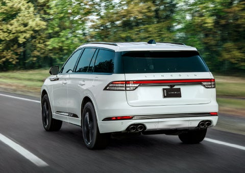 A white 2026 Lincoln Aviator® SUV is being driven away down a road lined with colorful trees. | Zeigler Lincoln of Kalamazoo in Kalamazoo MI