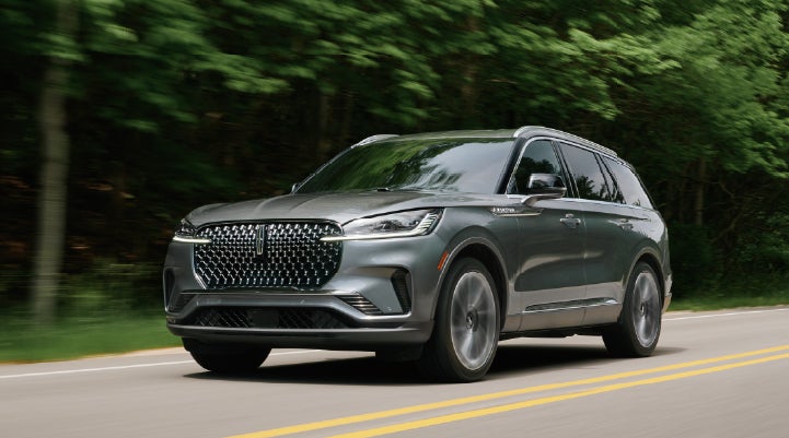 A 2027 Lincoln Aviator® SUV is being driven down a road lined with trees. | Zeigler Lincoln of Kalamazoo in Kalamazoo MI